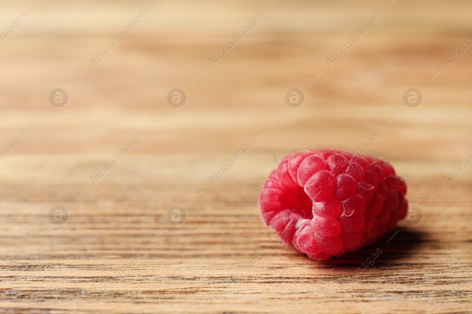 Photo of Delicious ripe raspberry on wooden table, closeup. Space for text