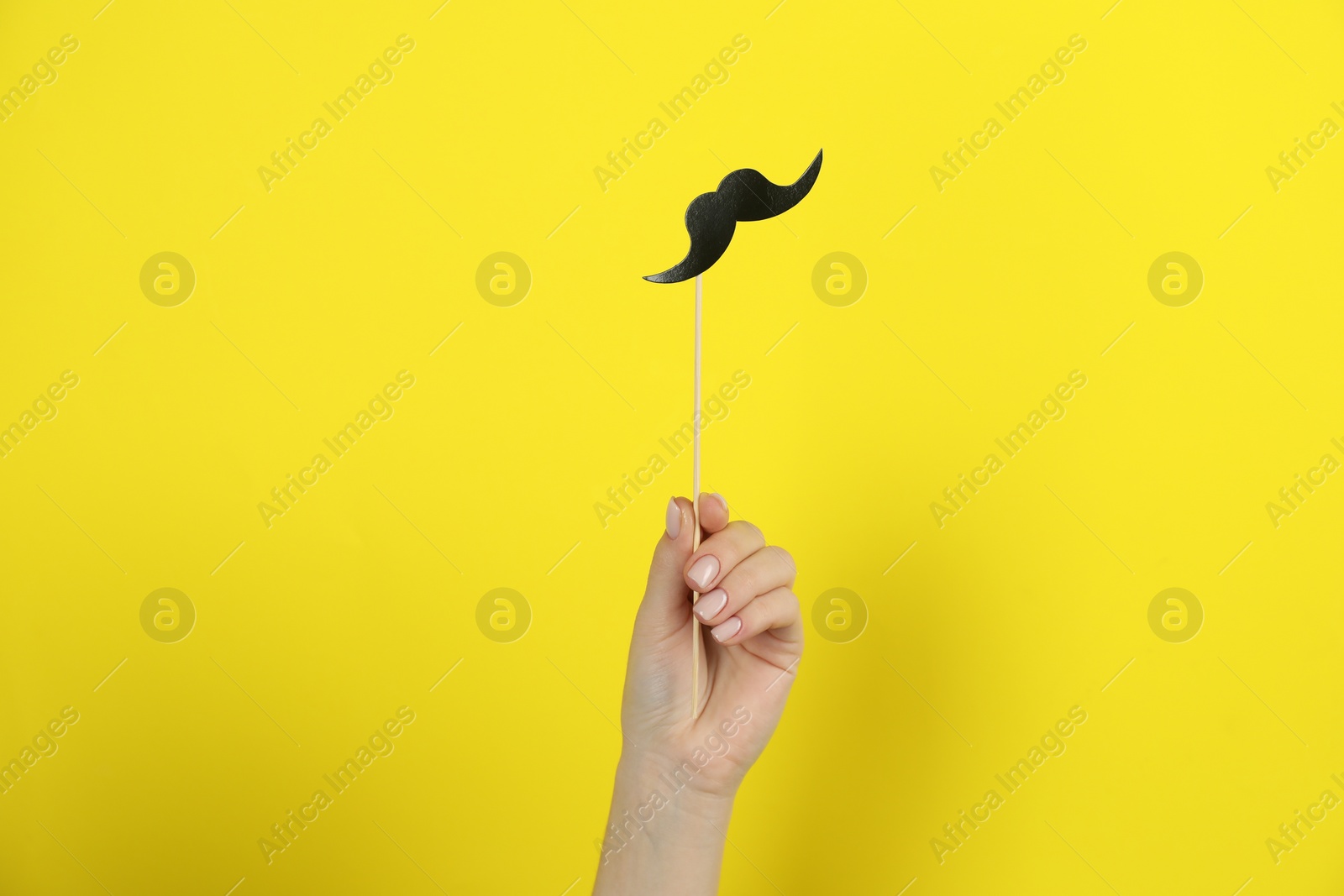 Photo of Woman with fake paper mustache on yellow background, closeup