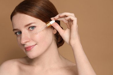 Photo of Beautiful woman with freckles applying cosmetic serum onto her face on beige background