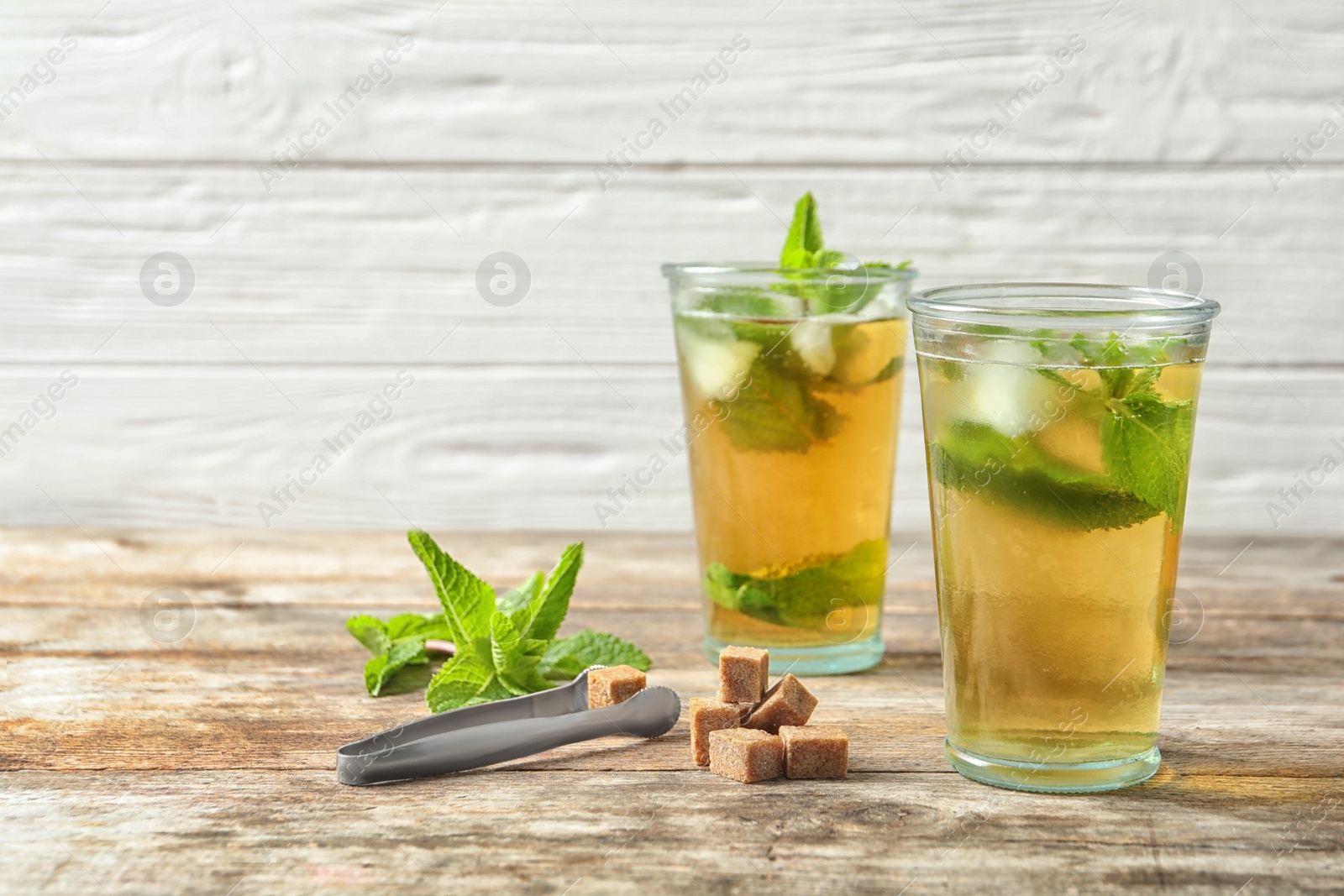 Photo of Glasses with aromatic mint tea, fresh leaves and sugar cubes on wooden table