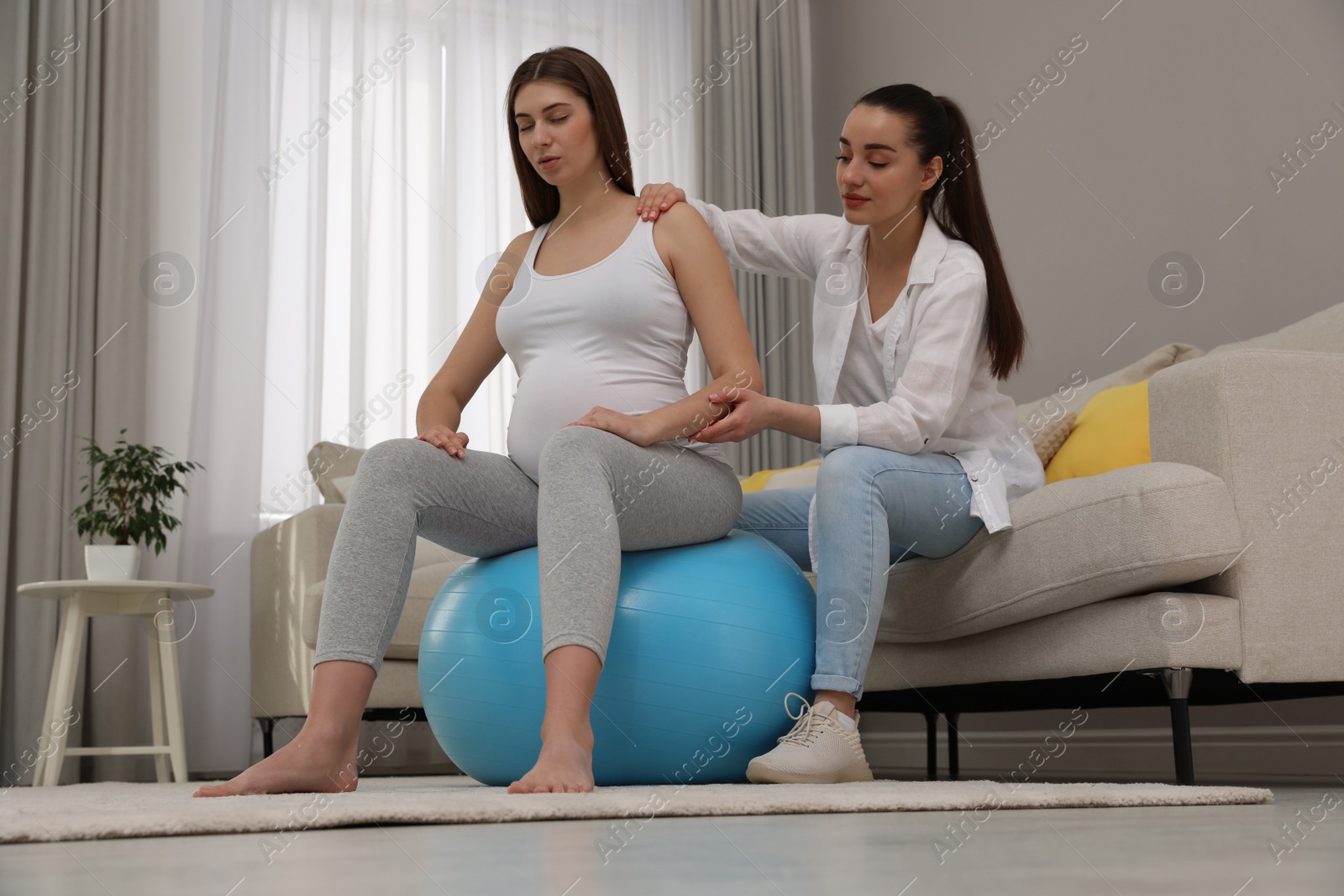 Photo of Doula working with pregnant woman in living room. Preparation for child birth