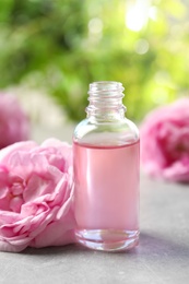 Photo of Bottle of rose essential oil and fresh flowers on grey table