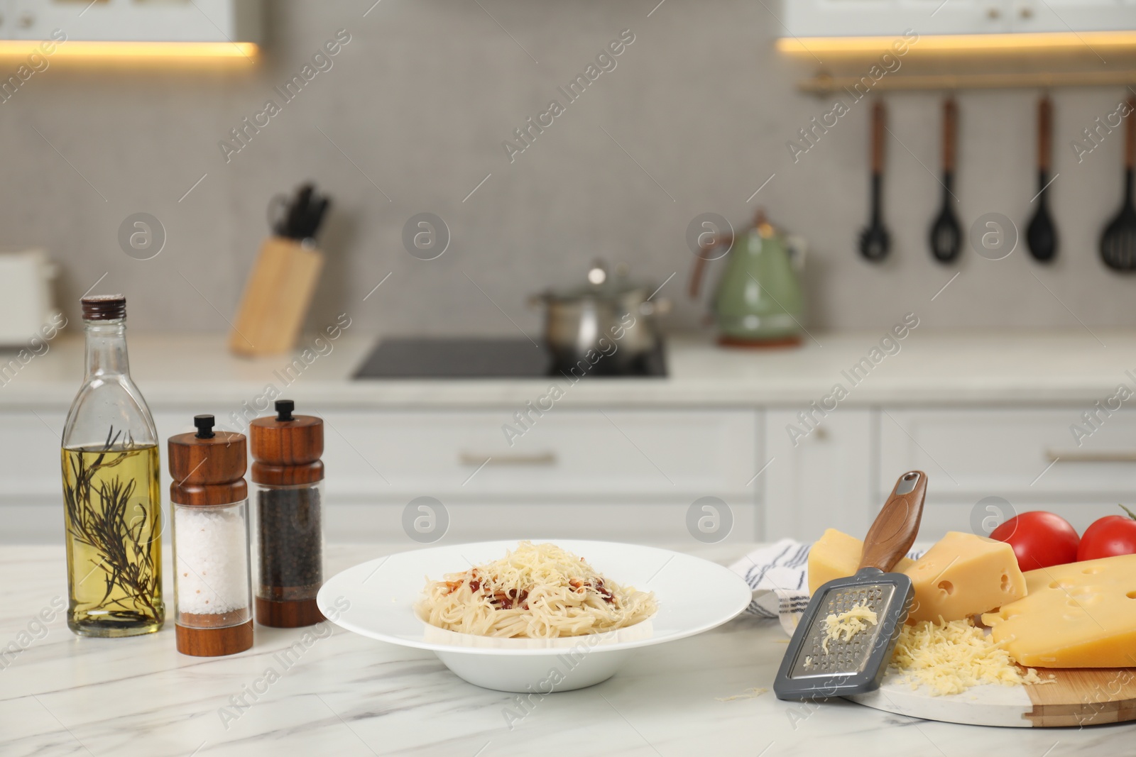 Photo of Delicious pasta with grated cheese and other products on white marble table in kitchen