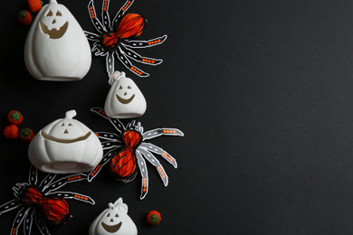 Image of White pumpkin shaped candle holders, paper spiders and jelly candies on black background, flat lay with space for text. Halloween decoration