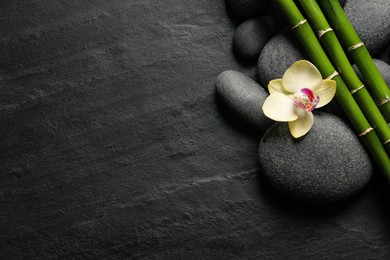 Photo of Spa stones, beautiful orchid flower and bamboo stems on black table, flat lay. Space for text