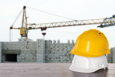 Image of Safety equipment. Hard hats on wooden surface near construction site with tower crane outdoors, space for text