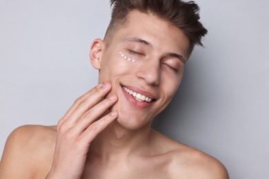 Photo of Handsome man with moisturizing cream on his face against light grey background