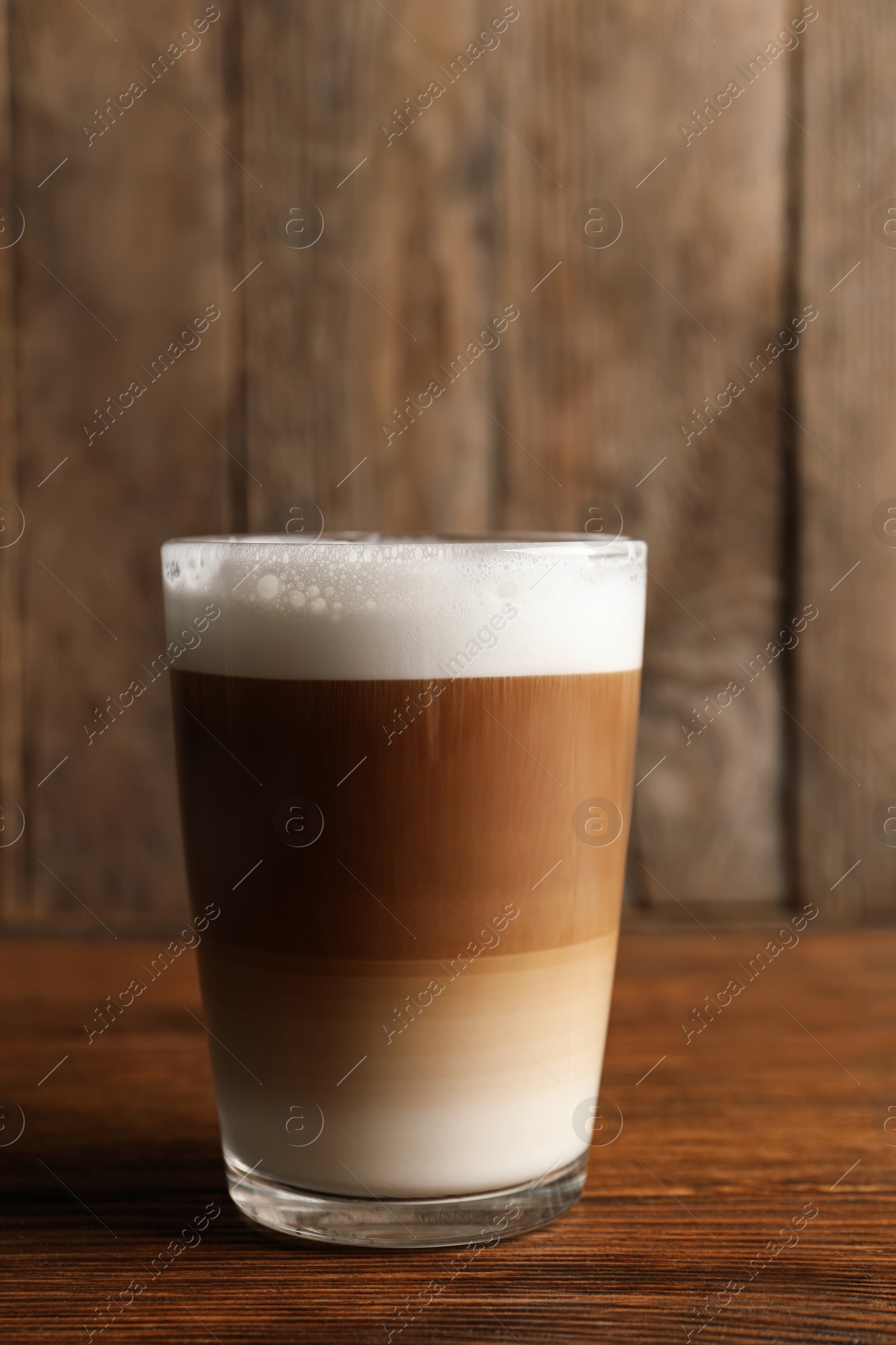 Photo of Glass of delicious layered coffee on wooden table, space for text