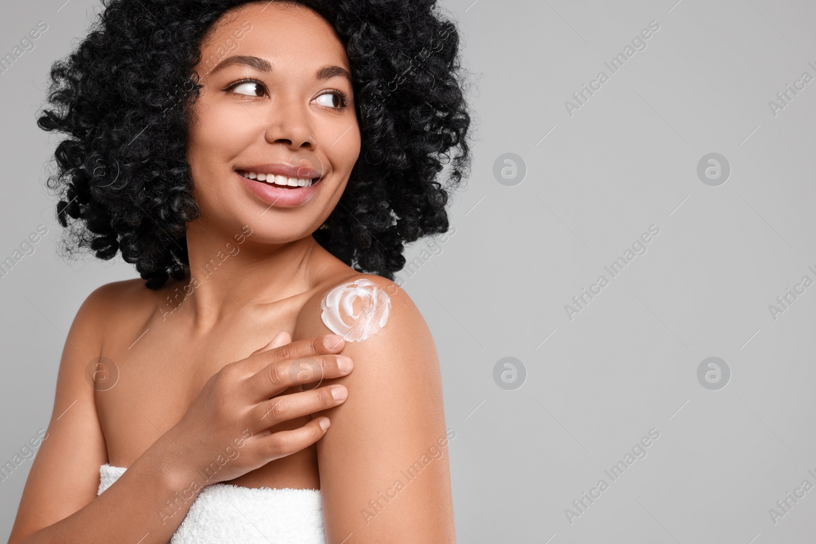 Photo of Young woman applying body cream onto shoulder on grey background. Space for text