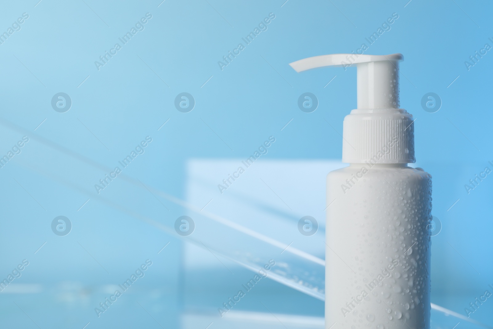 Photo of Wet bottle of face cleansing product on light blue background, closeup. Space for text