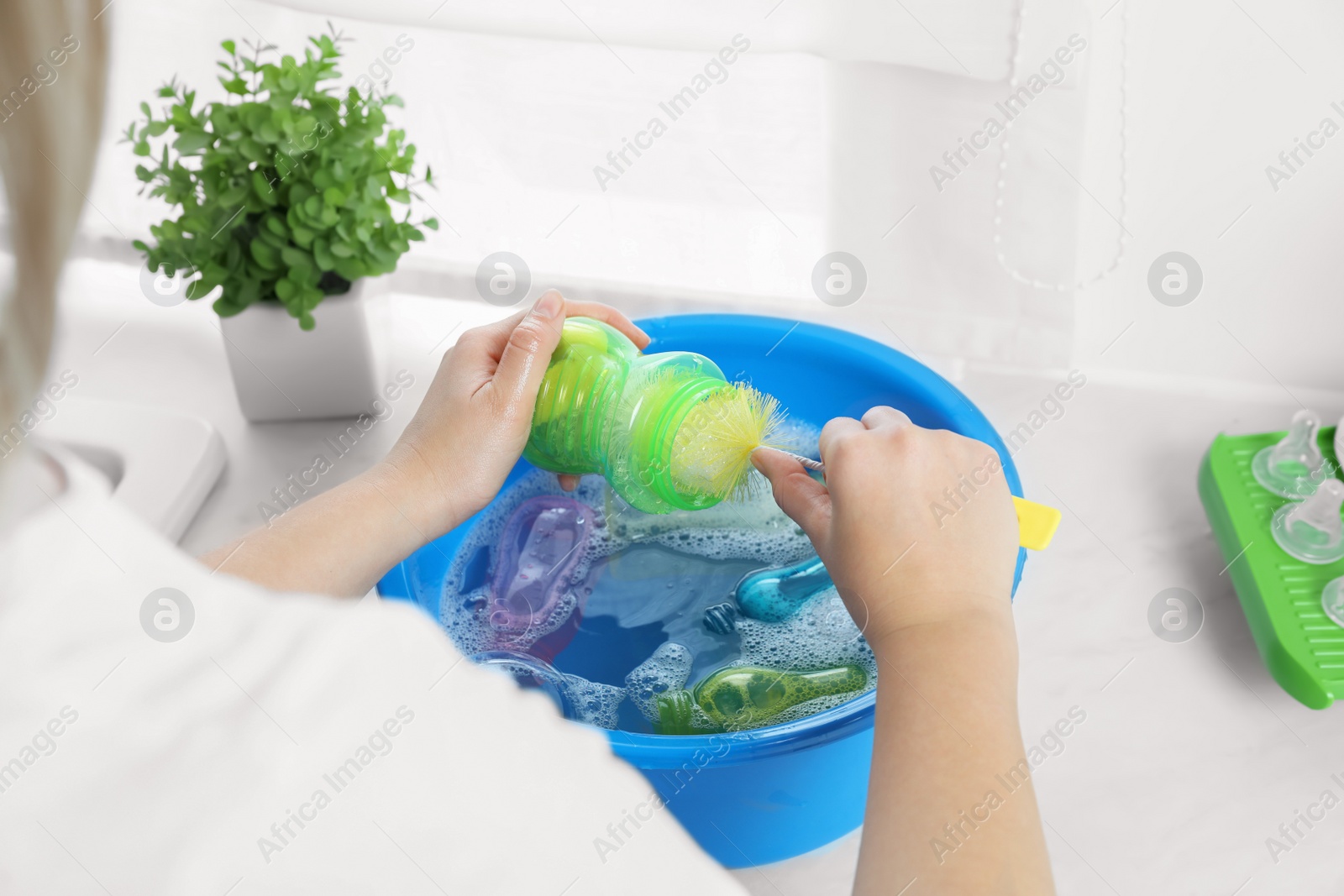 Photo of Woman washing baby bottle above basin in kitchen, closeup