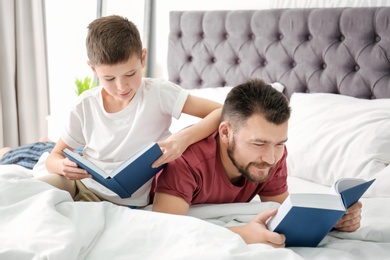 Photo of Little boy and his dad reading books in bedroom