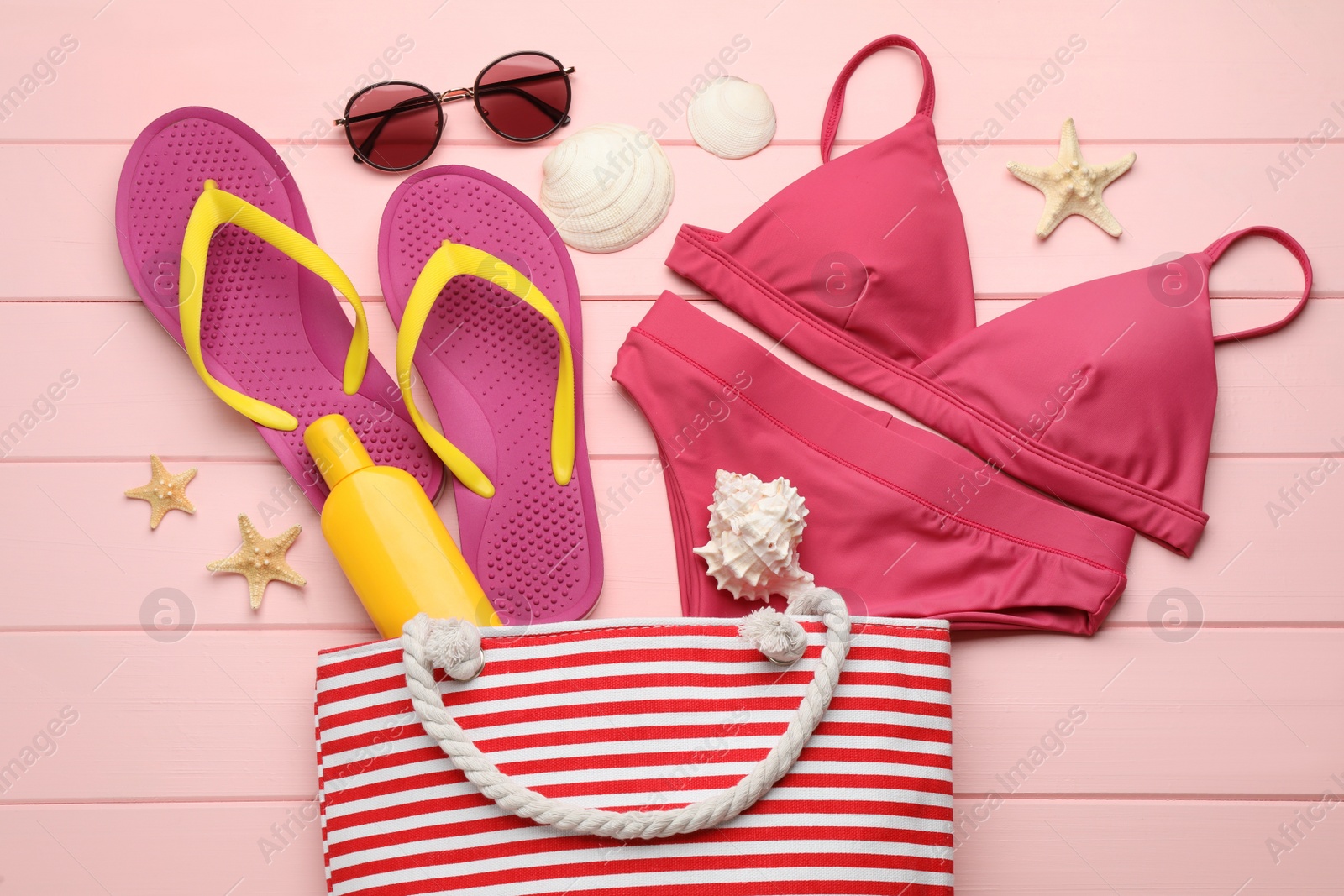 Photo of Stylish bag and beach accessories on pink wooden background, flat lay