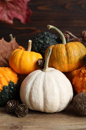 Photo of Thanksgiving day. Composition with pumpkins and conifer cones on wooden table, closeup