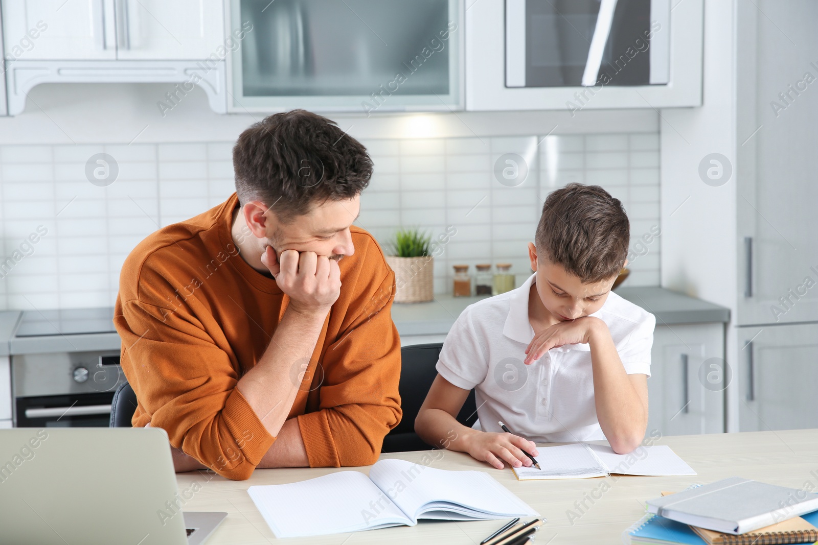 Photo of Dad helping his son with difficult homework assignment in kitchen