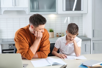 Photo of Dad helping his son with difficult homework assignment in kitchen