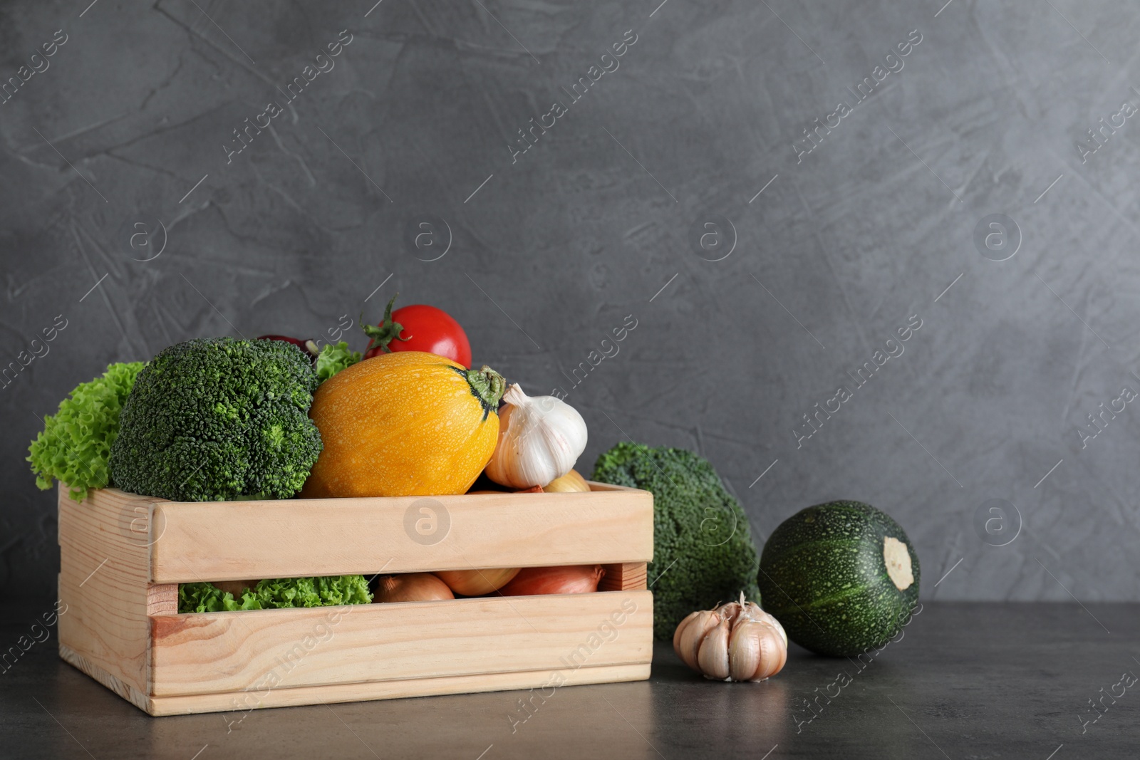 Photo of Wooden crate filled with delicious fresh vegetables on table against color background, space for text