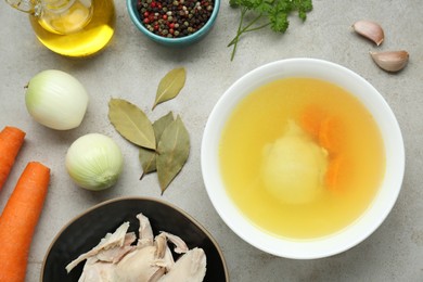 Photo of Delicious chicken bouillon and ingredients on light grey textured table, flat lay