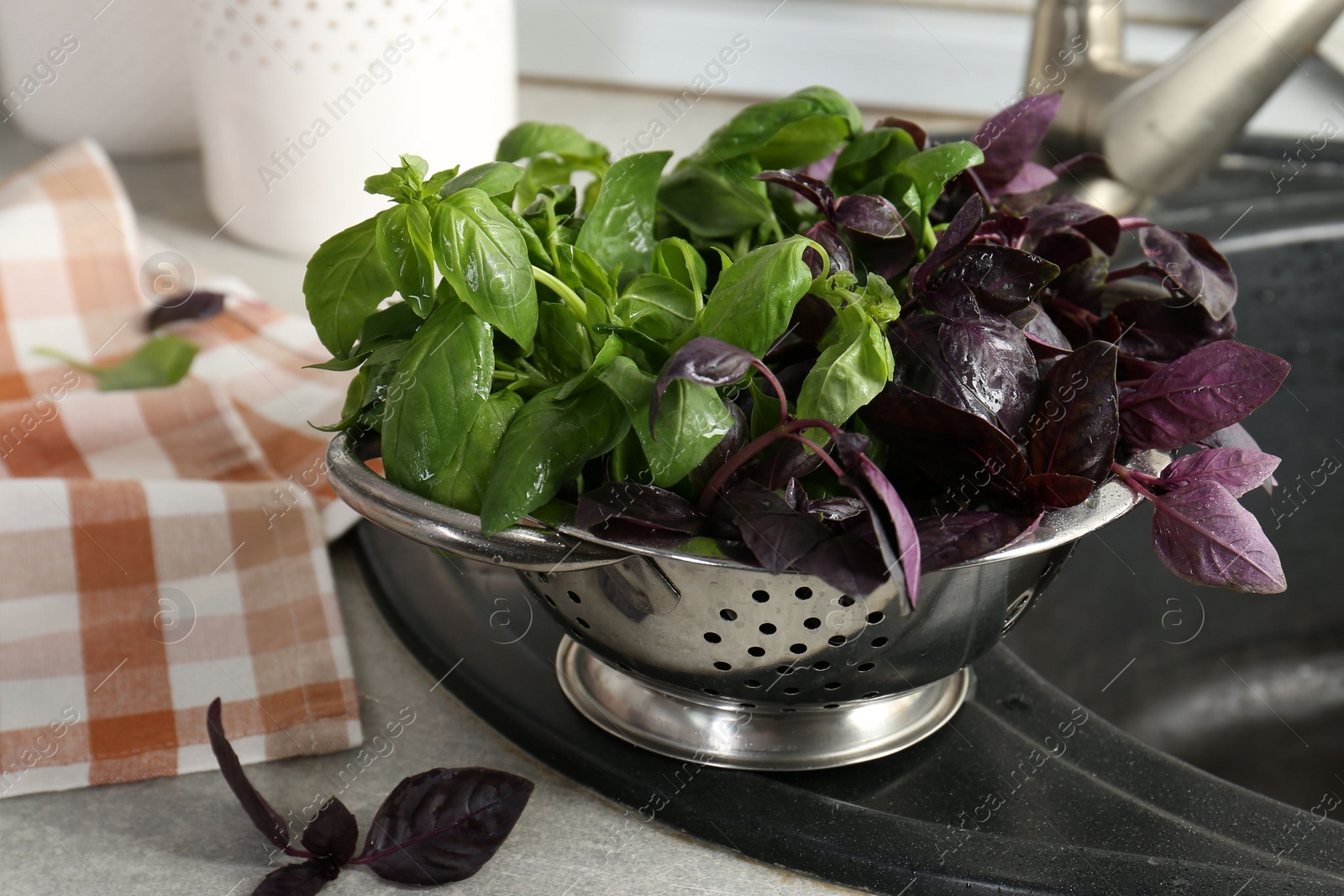 Photo of Metal colander with different fresh basil leaves on sink