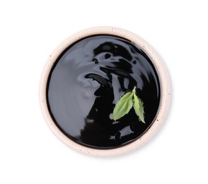 Balsamic glaze with basil leaves in bowl isolated on white, top view