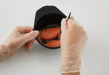 Photo of Woman preparing hair dye in bowl at white table, closeup