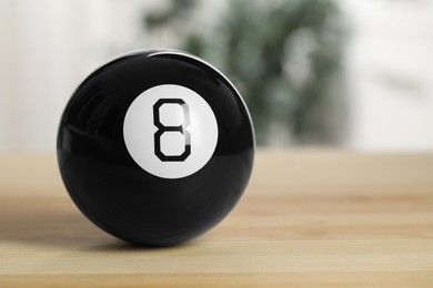 Photo of Magic eight ball with on wooden table, closeup. Space for text