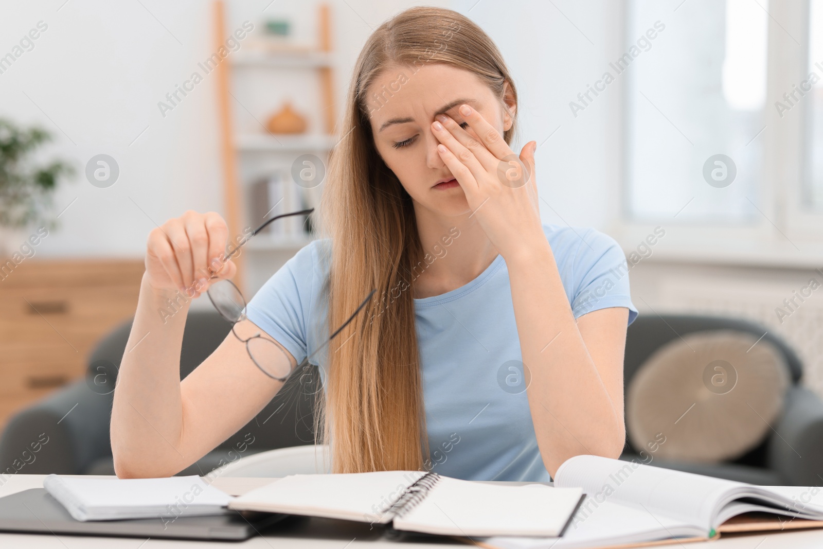 Photo of Overwhelmed young woman with glasses and books at table in room