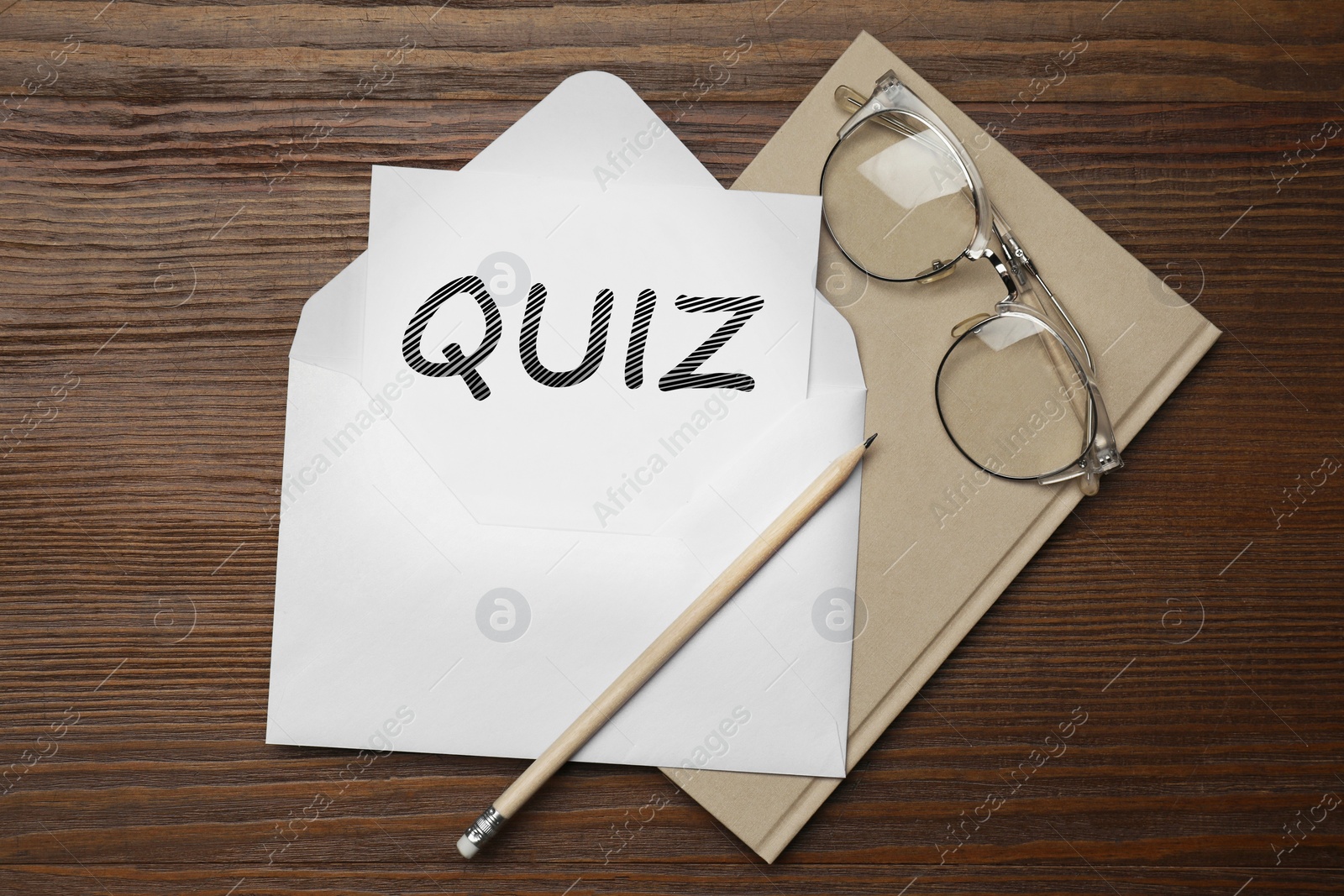 Image of Paper with words QUIZ in envelope, pencil, notebook and glasses on wooden table, flat lay