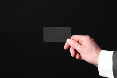 Businessman holding blank business card on black background, closeup. Space for text