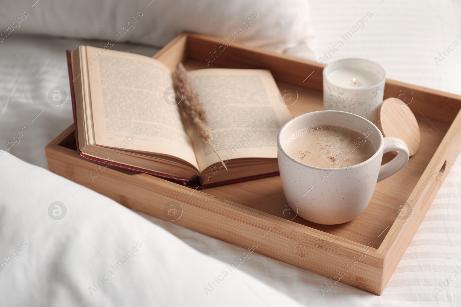 Photo of Cup of aromatic coffee, book and candle on white blanket, closeup