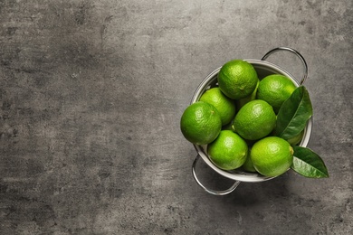 Photo of Colander with fresh ripe limes on gray background, top view
