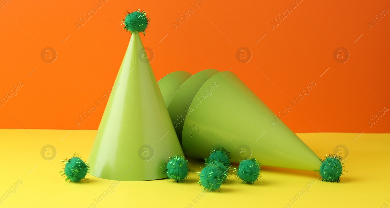 Photo of Party hats on yellow table against orange background