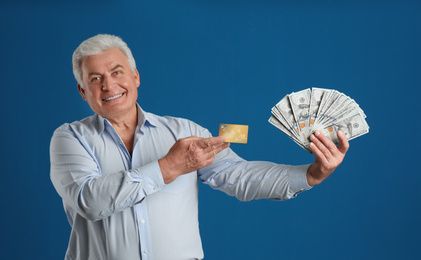 Happy senior man with cash money and credit card on blue background
