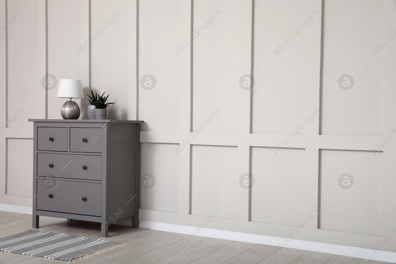 Photo of Grey chest of drawers near empty molding wall indoors, space for text