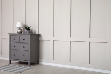 Photo of Grey chest of drawers near empty molding wall indoors, space for text