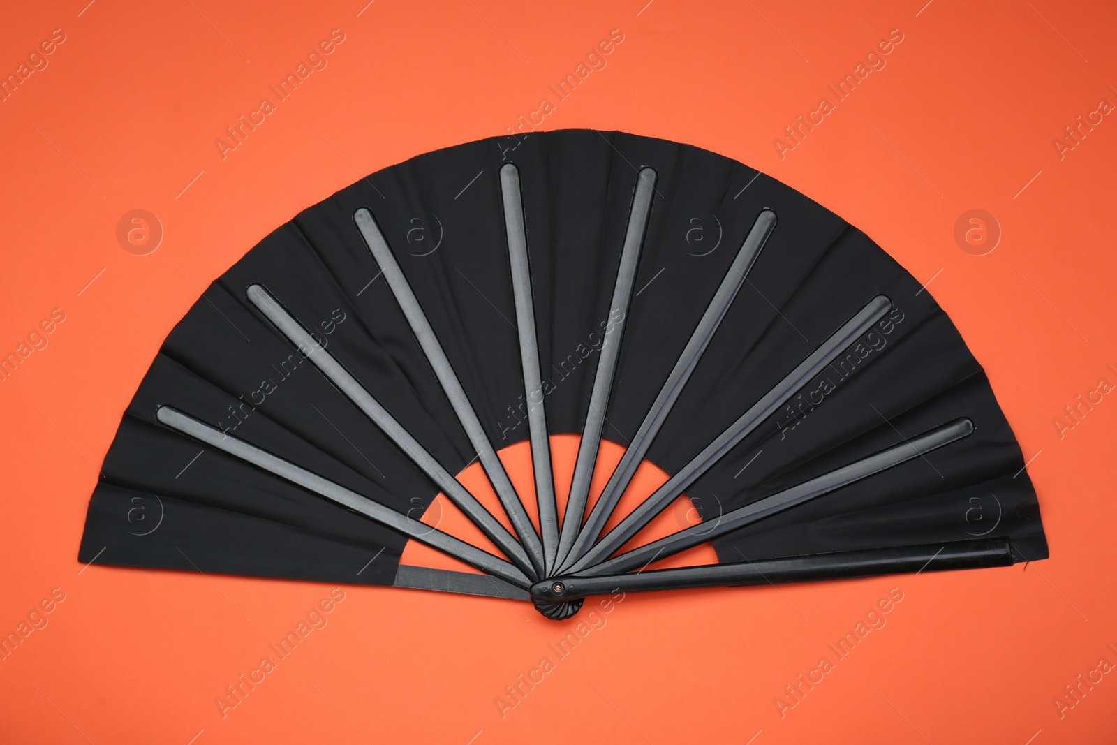 Photo of Stylish black hand fan on orange background, top view