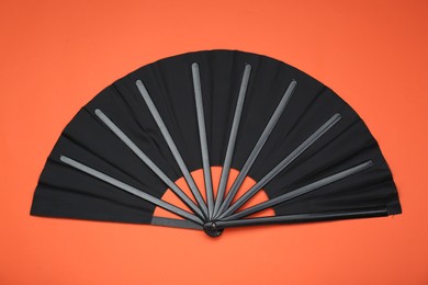 Photo of Stylish black hand fan on orange background, top view