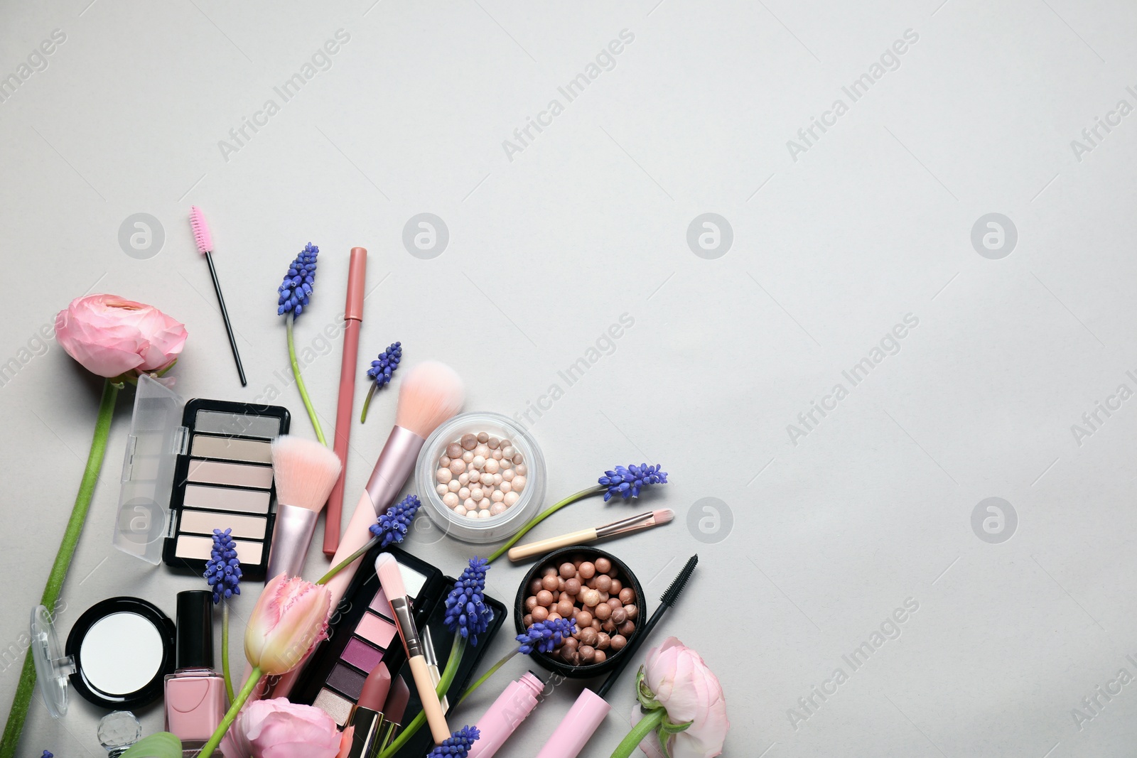 Photo of Flat lay composition with different makeup products and beautiful spring flowers on gray background, space for text