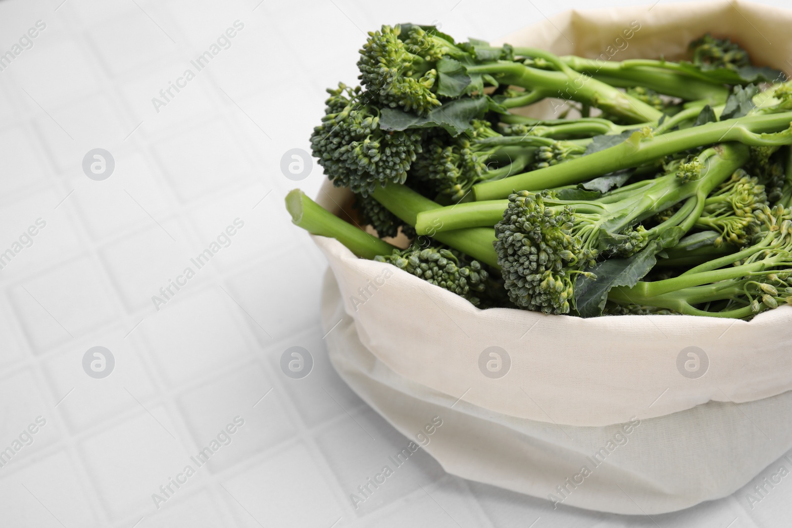 Photo of Bag with fresh raw broccolini on white tiled table, closeup and space for text. Healthy food