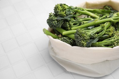 Bag with fresh raw broccolini on white tiled table, closeup and space for text. Healthy food