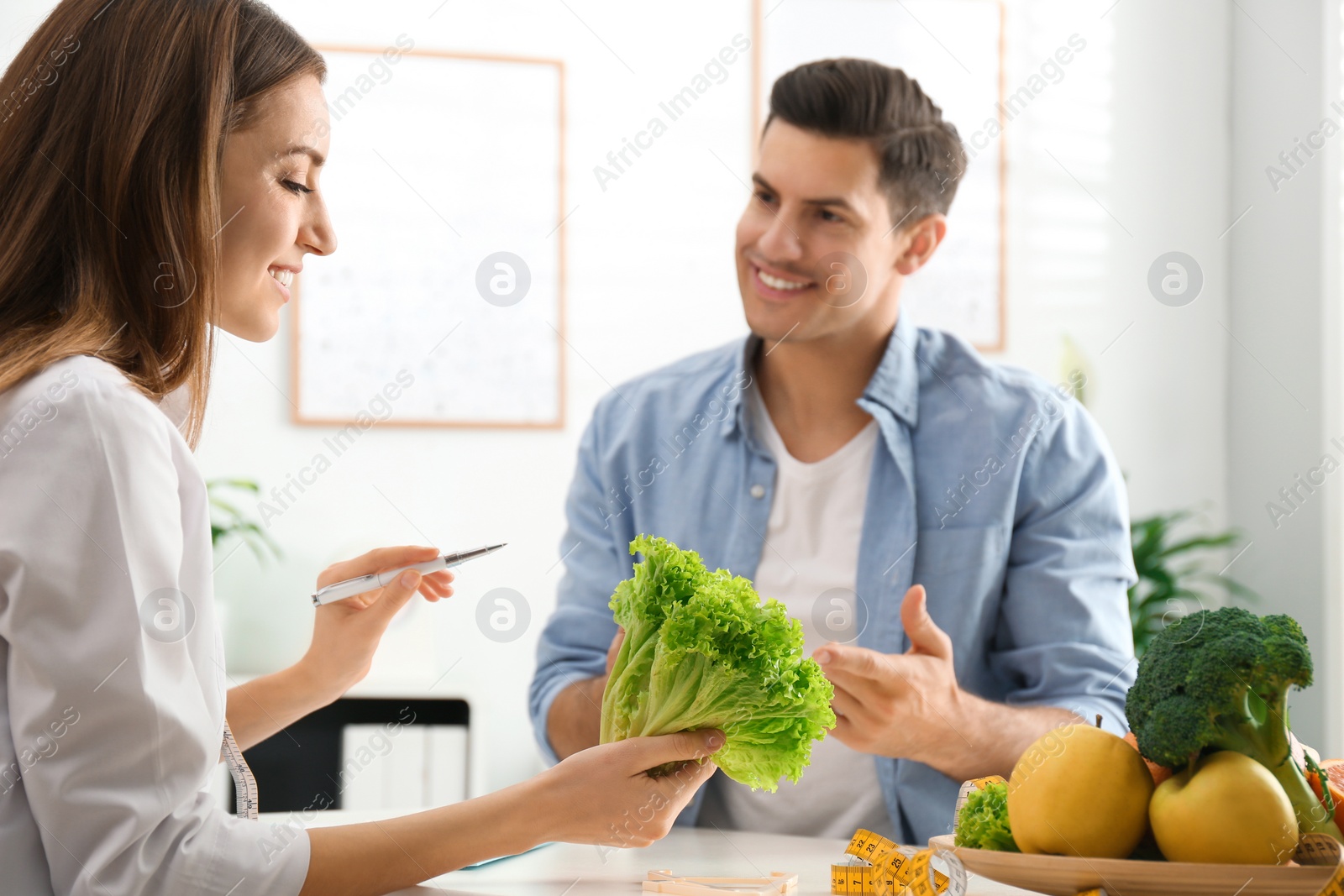 Photo of Young nutritionist consulting patient at table in clinic