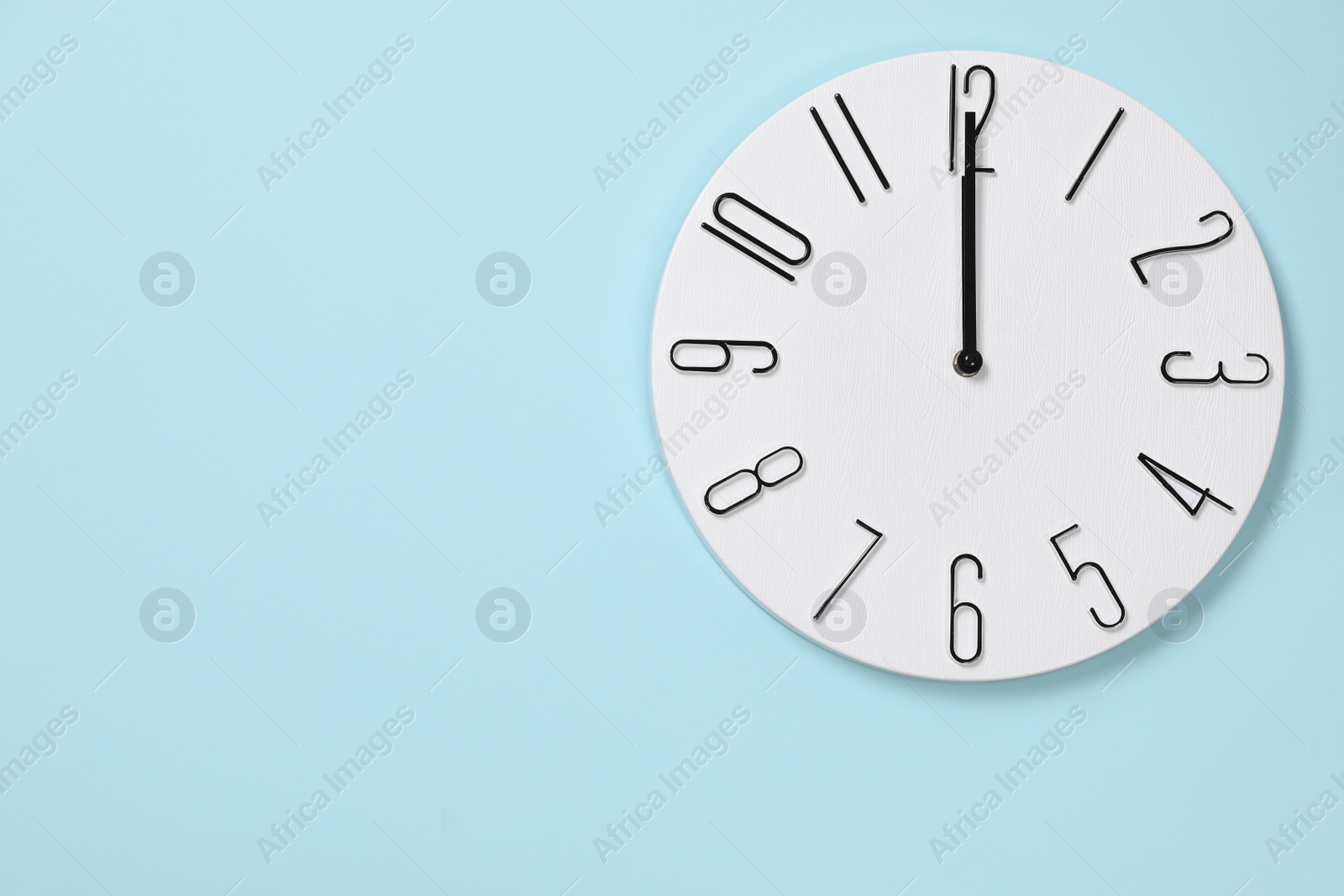 Photo of Stylish analog clock hanging on light blue wall, space for text