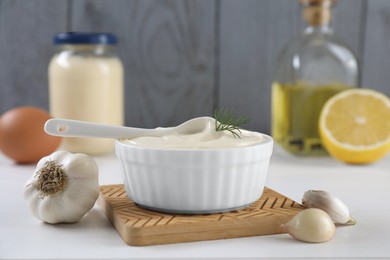 Fresh mayonnaise sauce in bowl and ingredients on white table