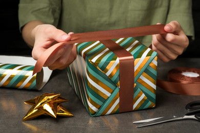 Photo of Woman wrapping gift at grey table, closeup