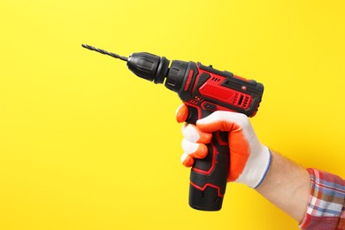 Handyman holding electric screwdriver on yellow background, closeup