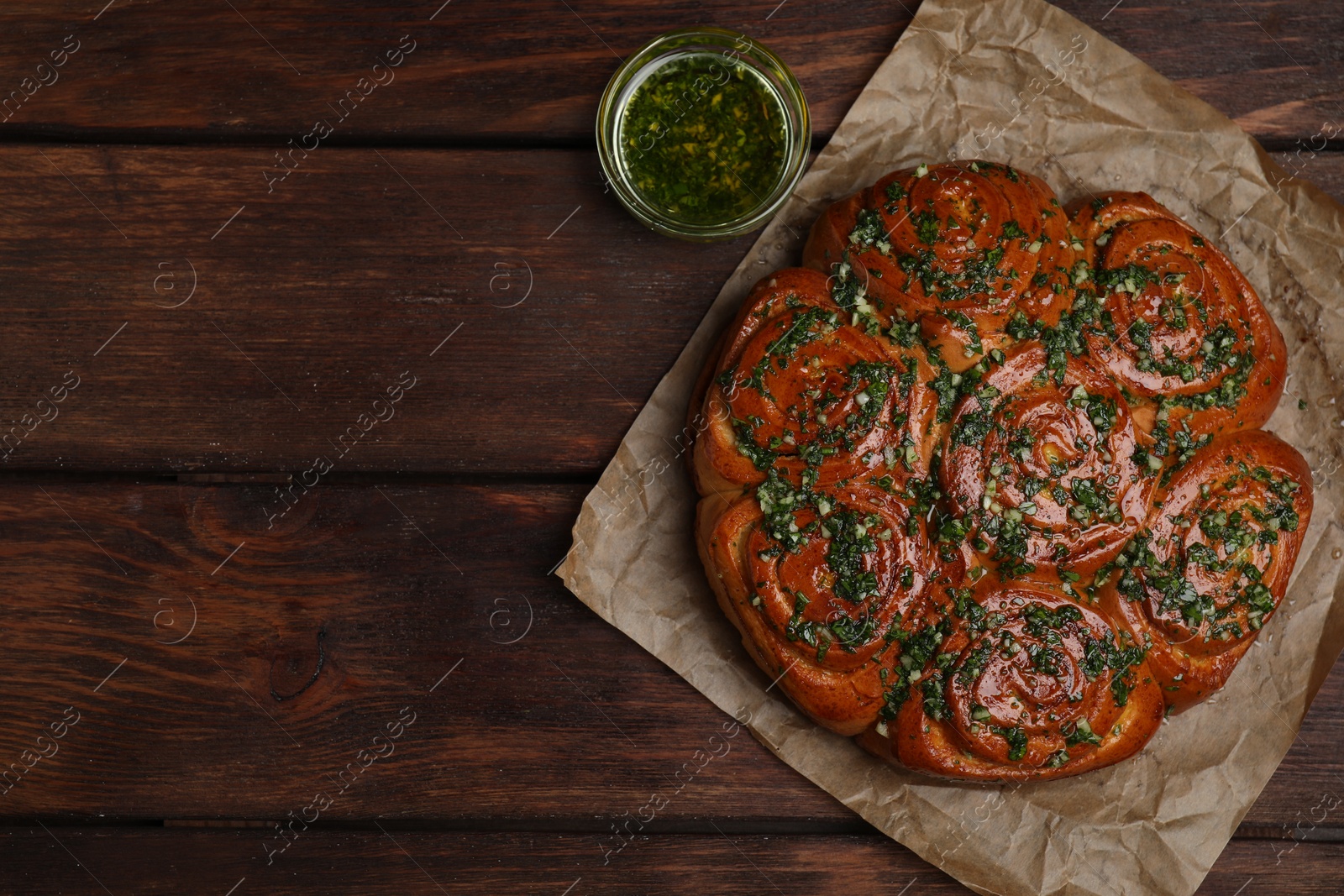Photo of Traditional Ukrainian garlic bread with herbs (Pampushky) and aromatic oil on wooden table, flat lay. Space for text