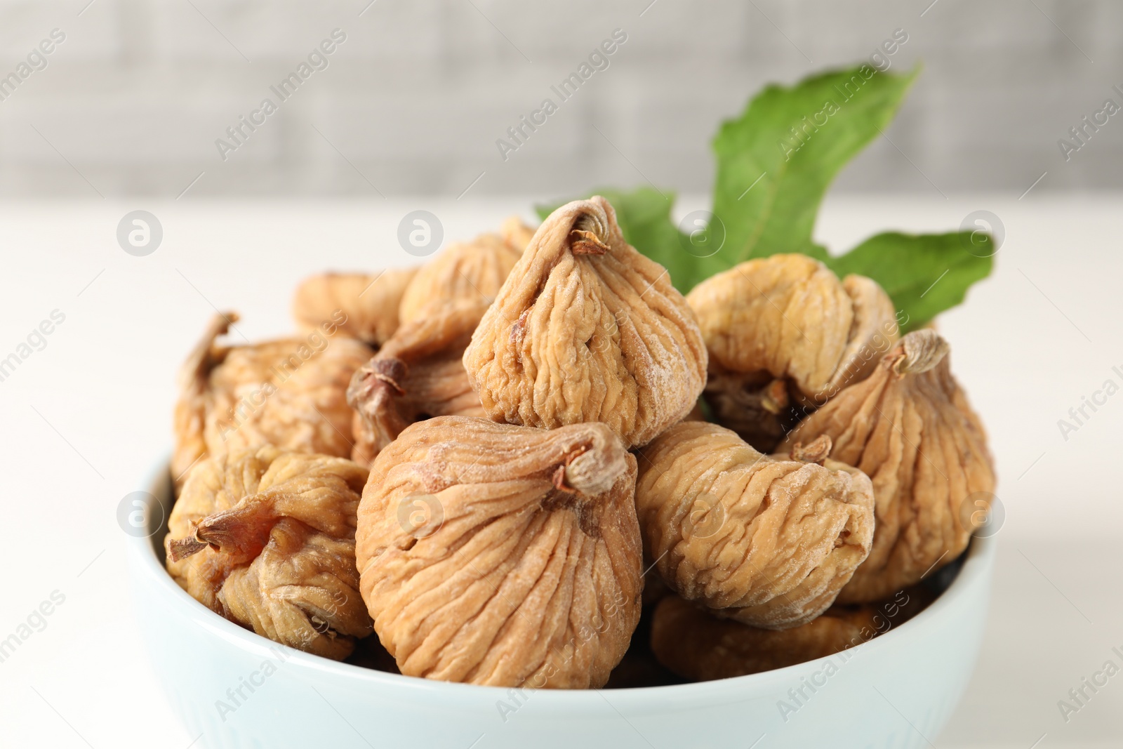 Photo of Bowl with tasty dried figs and green leaf on white table, closeup