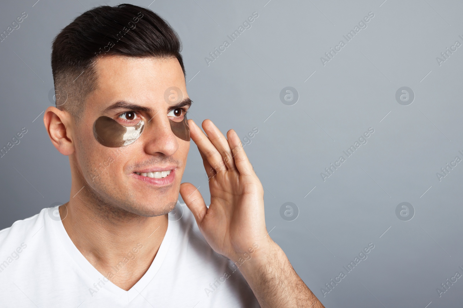 Photo of Man applying dark under eye patch on grey background. Space for text