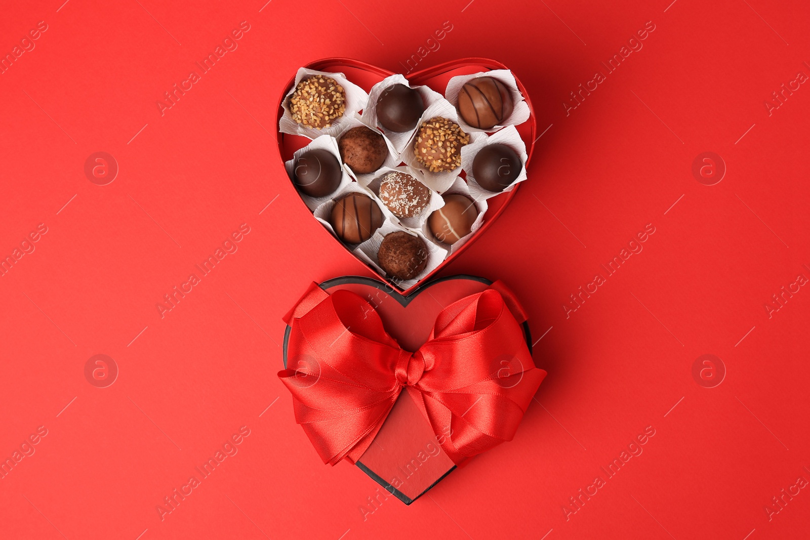 Photo of Heart shaped box with delicious chocolate candies on red table, flat lay