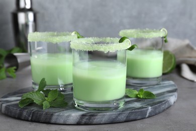 Photo of Delicious mint liqueur with ice cubes and green leaves on grey table